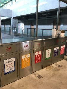 A row of five recycling bins, each for a different purpose.