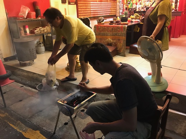 Man tending hibachi grill - in the background there is a small temple.