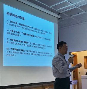 Speaker in front of a screen displaying Chinese writing.