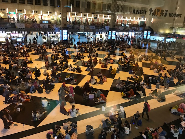 Many groups of people seated on the floor in a train station.