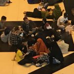 A group of people sitting on a train station floor.