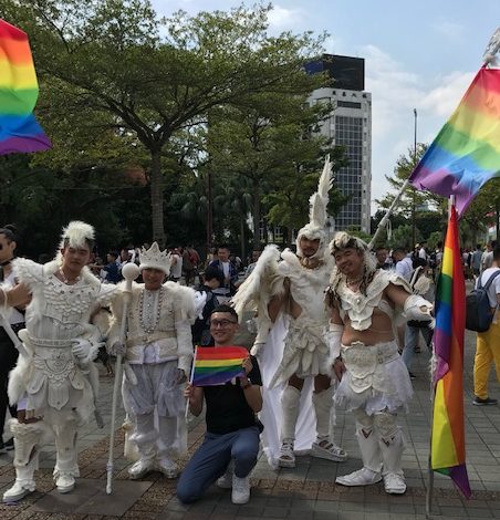Men in costumes posing with pride flags.
