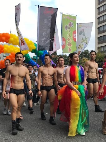 Person in a rainbow gown walking with men in ... very little.