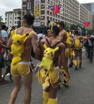 Two men in shorts with Pikachu backpacks and Pikachu ears.