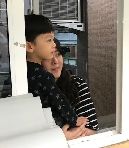 A small boy and his mother look through a window.