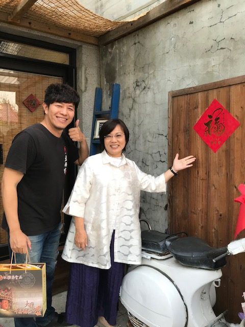 Two people gesturing toward a paper sign on a wall.