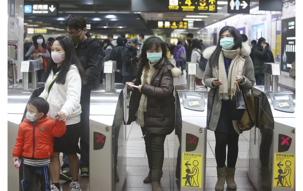 People entering a subway turnstile wearing medical face masks.